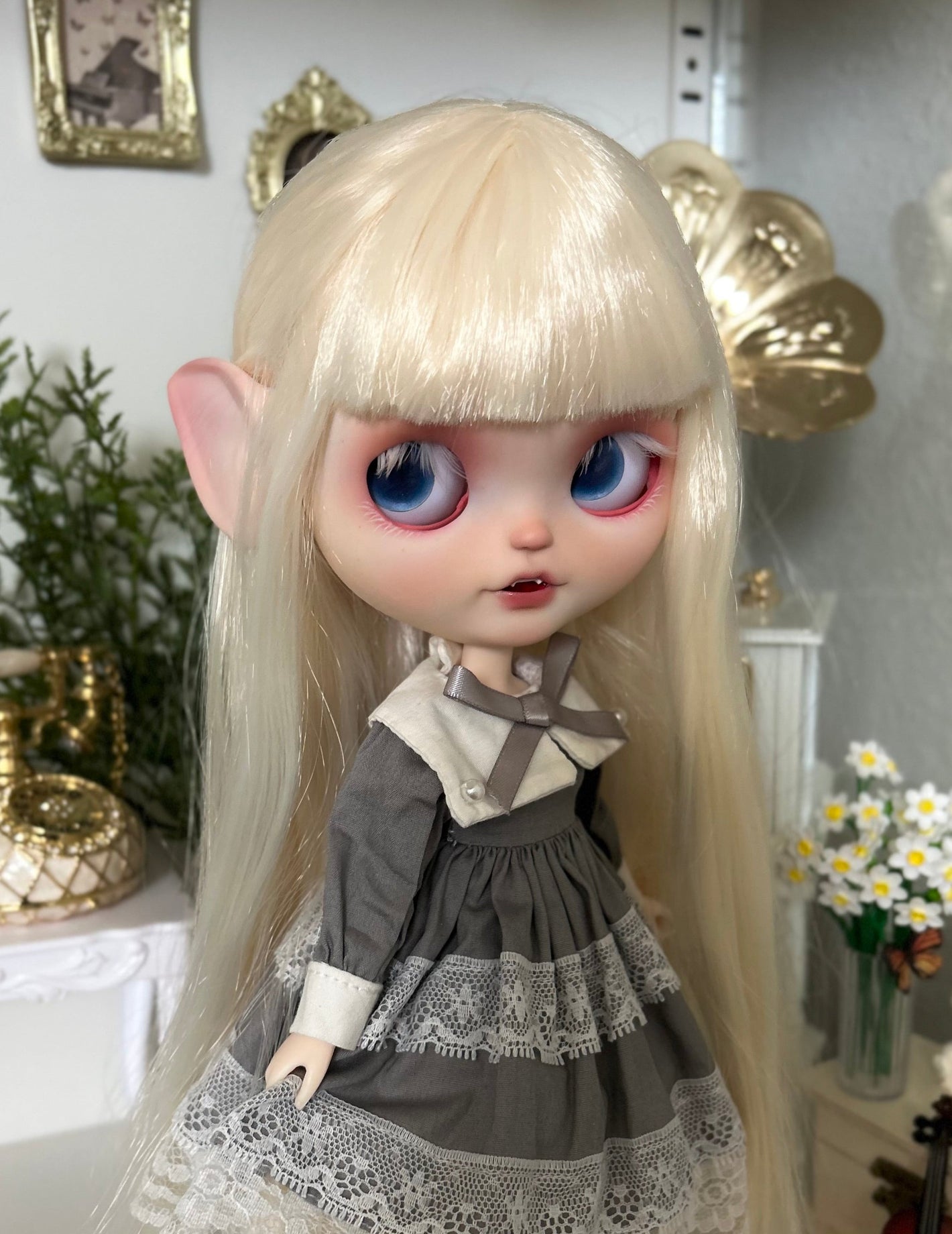 Doll with long blonde hair and blue eyes wearing a gray dress in a decorative setting.